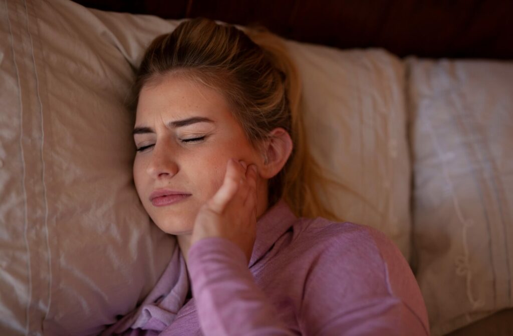Person lying against a pillow and holding the side of their face in discomfort.