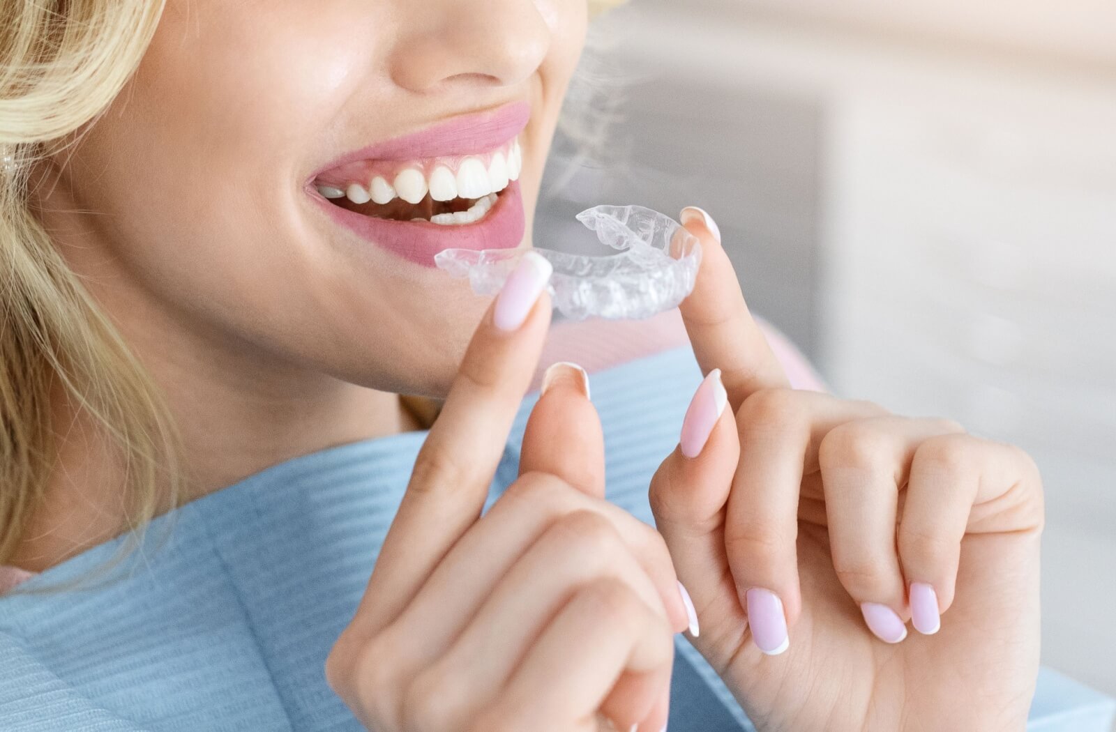 Close-up of a person smiling while holding a clear orthodontic aligner near their teeth
