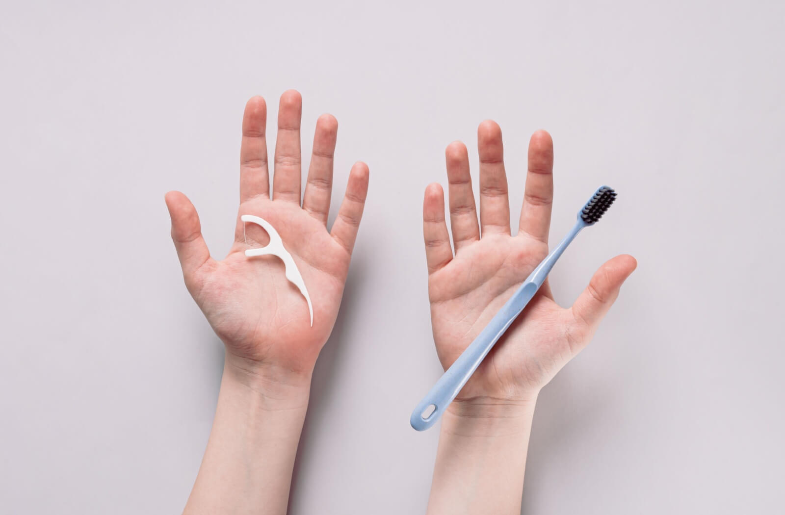 Open palms holding a floss pick and a manual toothbrush.